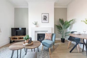 A living room with a fireplace, a television, a dining table, and a large plant. - Spacious 2BR Near Leeds Centre – Free Parking (Leeds)
