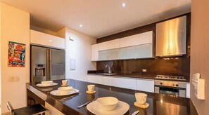Une cuisine moderne dotée d’un îlot central, d’appareils électroménagers en acier inoxydable et de meubles de rangement blancs.