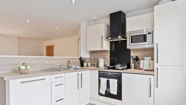 A modern kitchen with white cabinetry, a black range hood, a microwave, and an oven. - #90 The Lux Mint apartment JQ (West Midlands)