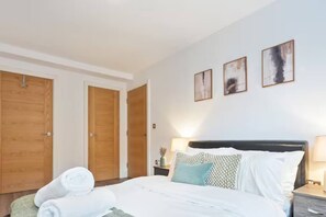 A hotel room with a bed, two wooden doors, a nightstand with a lamp, and three wall-mounted pictures. - #90 The Lux Mint apartment JQ (West Midlands)