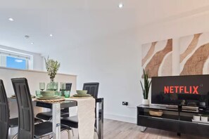 A modern dining area with a table set for two, a television on a stand, and a wall with a large Netflix logo. - #90 The Lux Mint apartment JQ (West Midlands)