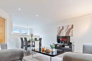 A modern living room with a dining area, a flat-screen TV, and a coffee table with books and a plant. - #90 The Lux Mint apartment JQ (West Midlands)