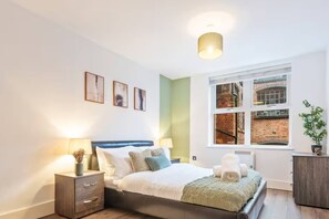 A modern bedroom with a bed, bedside tables, a window with a view of a brick building, and wall-mounted artwork. - #90 The Lux Mint apartment JQ (West Midlands)