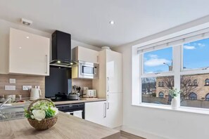 A modern kitchen with white cabinetry, a microwave, and a view of a building through a large window. - #90 The Lux Mint apartment JQ (West Midlands)
