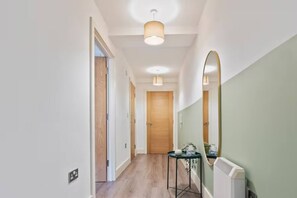 A hallway with a wooden door at the end, a small table with a plant, and a radiator on the wall. - #90 The Lux Mint apartment JQ (West Midlands)
