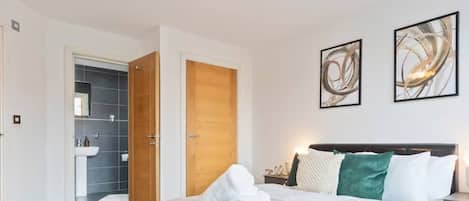 Une chambre moderne comprenant un lit, une table de chevet, une commode, une lampe fixée au mur et deux tableaux abstraits.