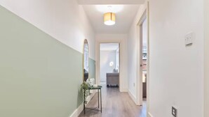 A hallway with a light fixture, a mirror, and a small table with a plant. - #90 The Lux Mint apartment JQ (West Midlands)