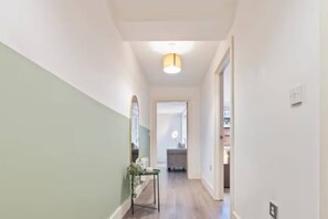 A hallway with a light fixture, a mirror, and a small table with a plant. - #90 The Lux Mint apartment JQ (West Midlands)