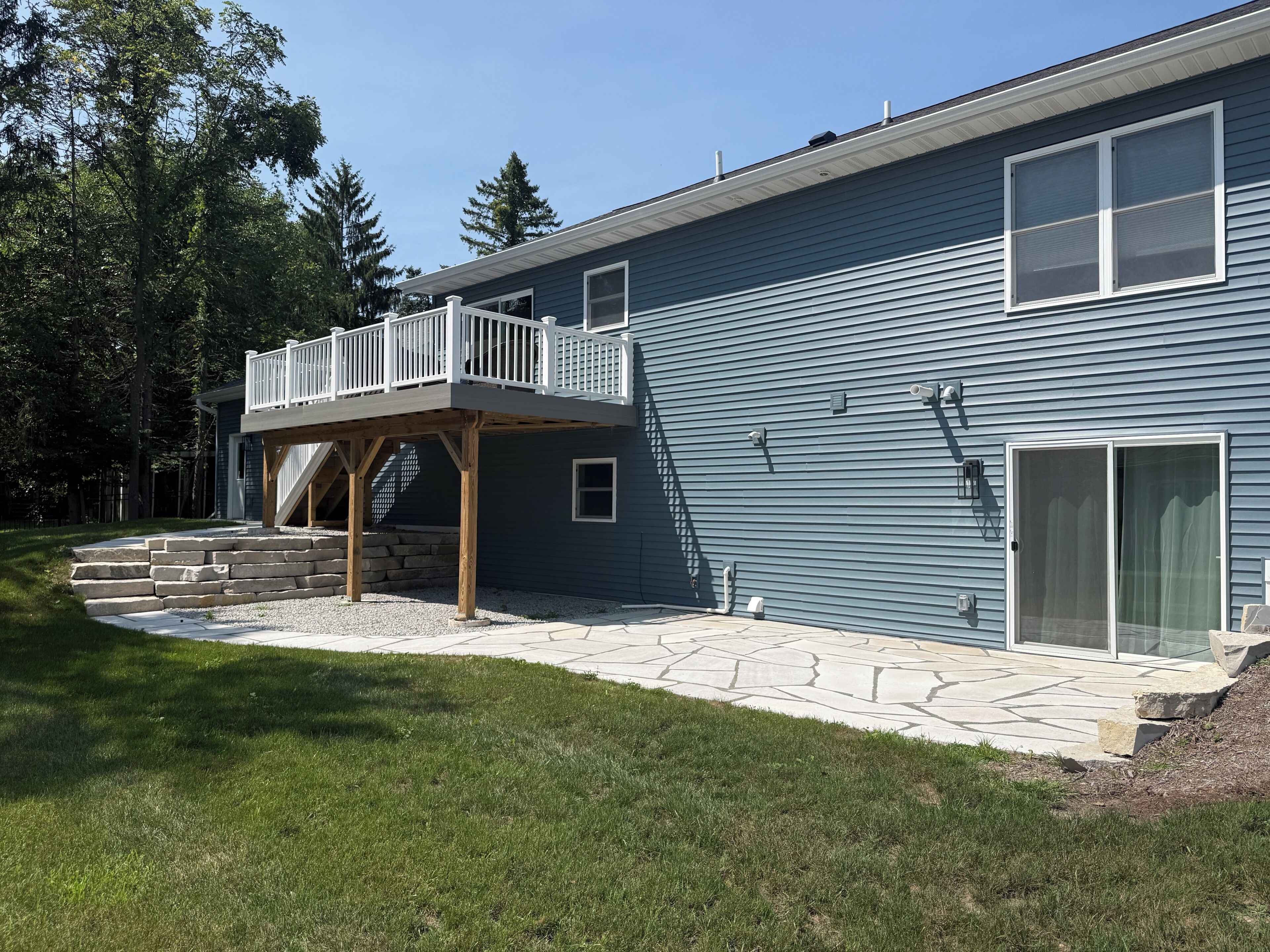 A two-story house with a wooden deck and stone steps leading to a front door.