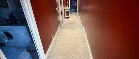 A narrow hallway with carpeted flooring and red walls.