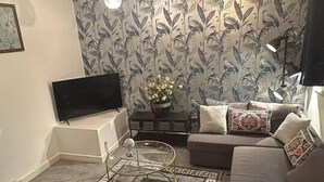 Ein Wohnzimmer mit Flachbildfernseher, einer Couch, einem Couchtisch und Wandpapier mit Muster.