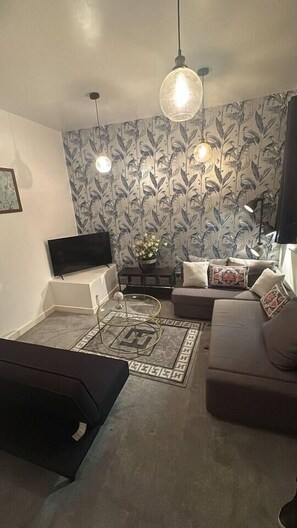 A living room with a flat-screen TV, a sofa, a coffee table, and patterned wallpaper. - #84 Large JQ apartment sleeps 9 (West Midlands)