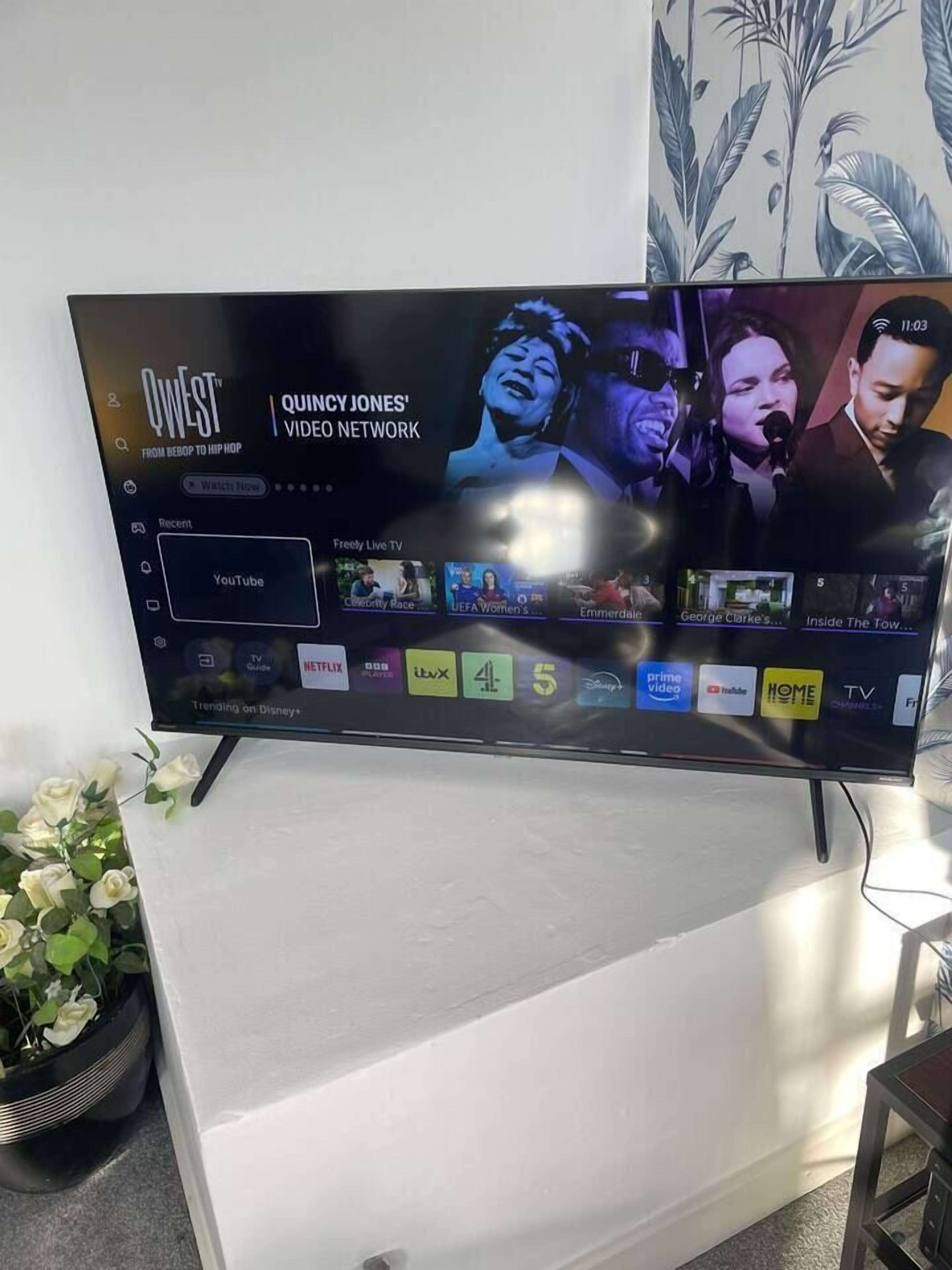 A flat-screen TV mounted on a white stand, displaying a video streaming service interface with various content options.
