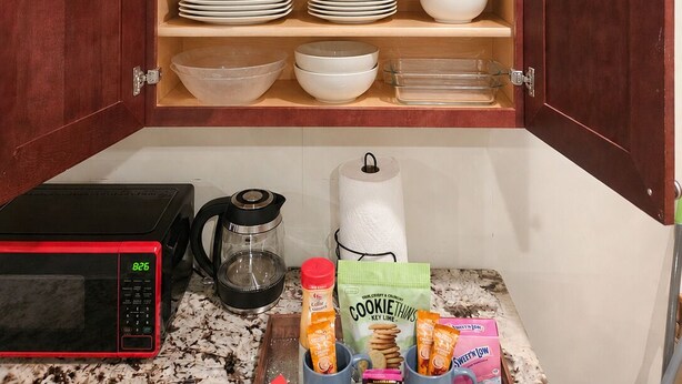 Una cocina con microondas, cafetera y distintos utensilios de cocina sobre la encimera.