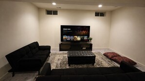 Una sala de estar con un televisor de pantalla plana, dos sofás negros, una mesa de centro y un tapete estampado.