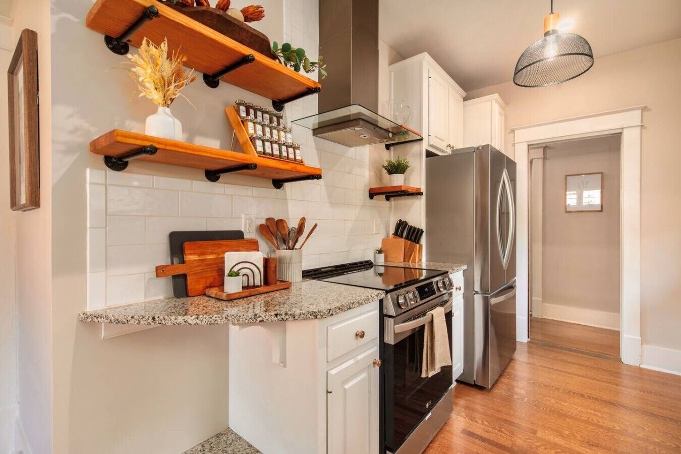 A kitchen with a granite countertop, stainless steel appliances, wooden shelves, and a hanging light fixture.