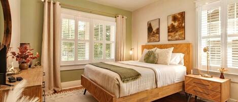 Une chambre à coucher avec un lit en bois, des tables de chevet, une commode, une fenêtre avec des stores et une lampe fixée au mur.