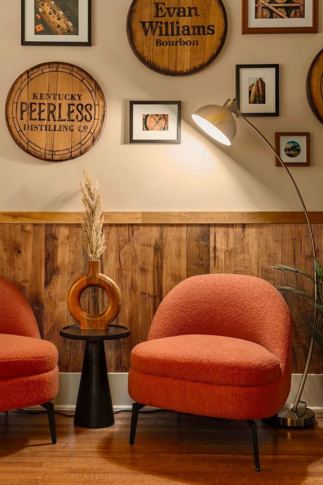 Una habitación con dos sillas naranjas, una decoración de pared con barril de madera y un cuadro con un reloj.