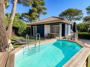 A swimming pool with a wooden deck, lounge chairs, and a covered patio area with a table and chairs.