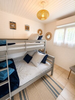 A bunk bed room with a hanging light fixture, a window with sheer curtains, and a wall-mounted mirror.