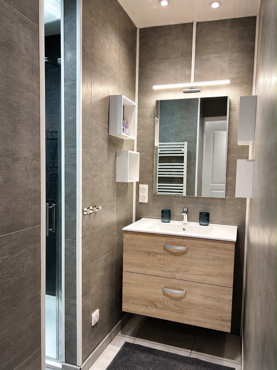 Une salle de bain moderne avec une douche à parois de verre, un meuble-lavabo en bois avec un miroir et un porte-serviettes intégré.