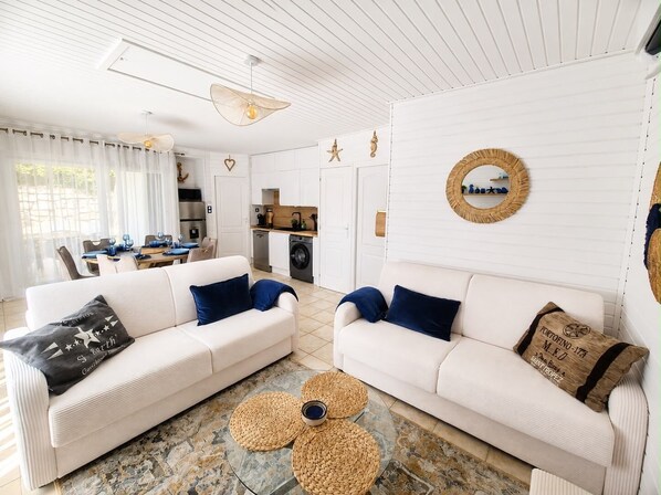 A modern living room with two white sofas, a dining area, and a kitchen.