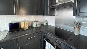 A modern kitchen with dark cabinetry, a stainless steel range hood, a toaster, and a kettle. - Romford Retreat - Modern 2 Bedroom Apartment (Romford)