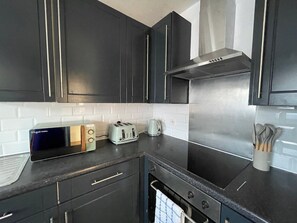 Eine moderne Küche mit dunklen Schränken, einer Edelstahl-Dunstabzugshaube, einem Toaster und einem Wasserkocher.