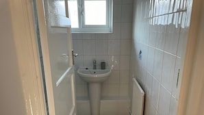 A small bathroom with a white sink, a window, and a radiator. - Romford Retreat - Modern 2 Bedroom Apartment (Romford)