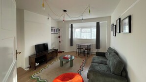 A living room with a sofa, a television, a small table, and a floor lamp. - Romford Retreat - Modern 2 Bedroom Apartment (Romford)