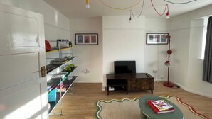 A room with a television, a bookshelf, a desk with a lamp, and a patterned rug. - Romford Retreat - Modern 2 Bedroom Apartment (Romford)
