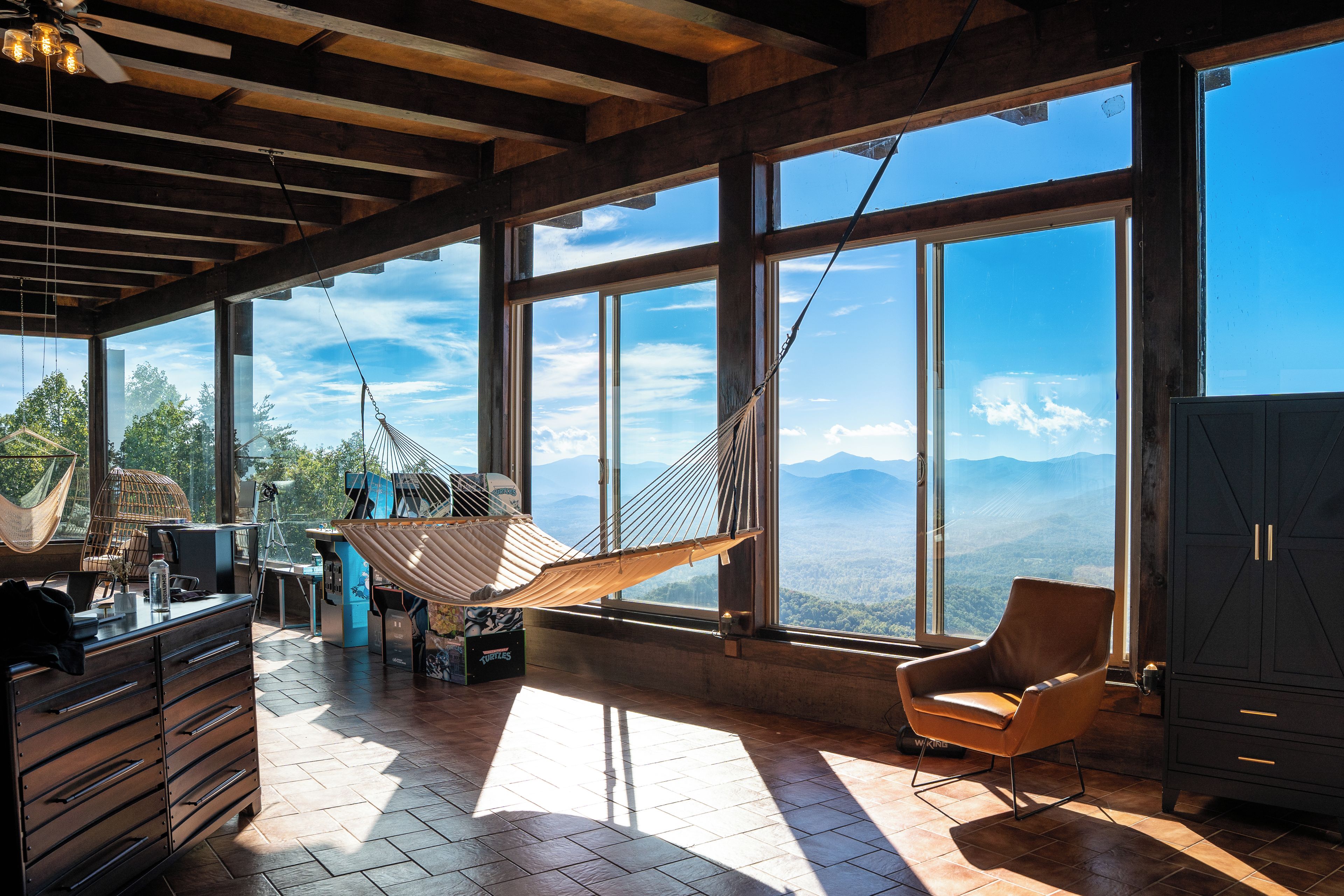 A spacious room with large windows, a hammock, a chair, and a desk with a computer.