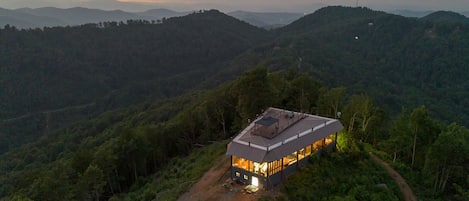 Un edificio de una sola planta con techo plano, rodeado de un bosque denso y un sendero de tierra que conduce a la entrada.