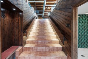 A staircase with wooden walls and a tiled floor leading to a room with a green patterned wall.