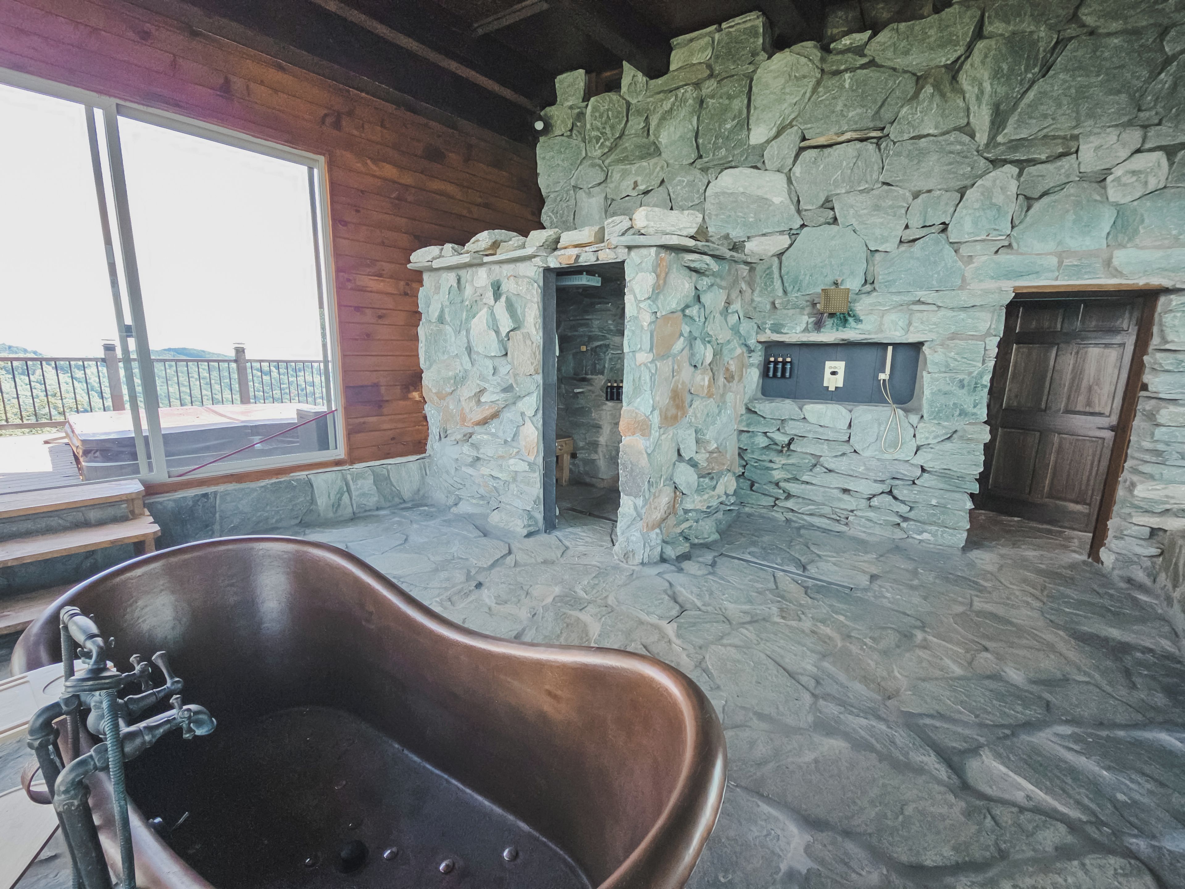 A stone-walled bathroom with a freestanding bathtub, a shower area, and a wooden door.