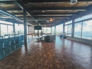 Un vaste espace intérieur comprenant un bar, des sièges et de grandes fenêtres donnant sur un paysage.