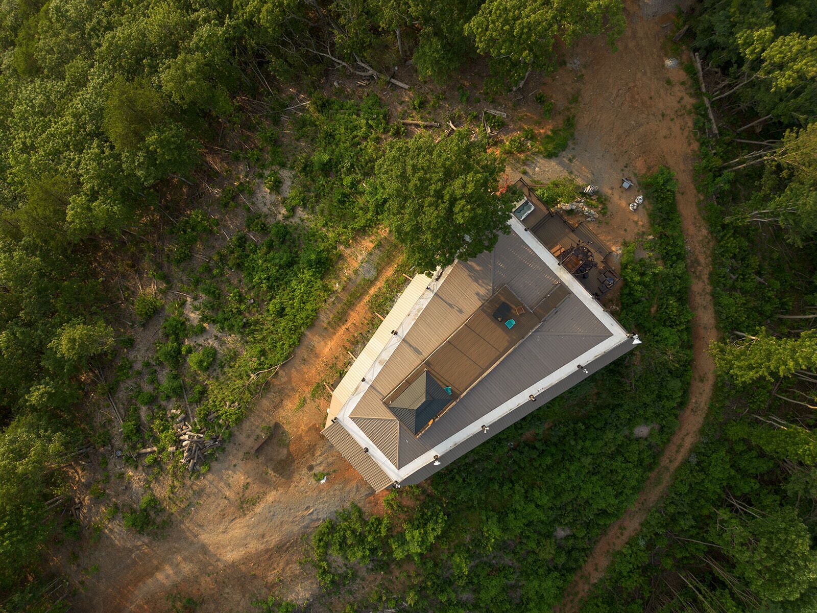Vista aérea de um edifício retangular com telhado plano, cercado por vegetação densa e um caminho de terra.