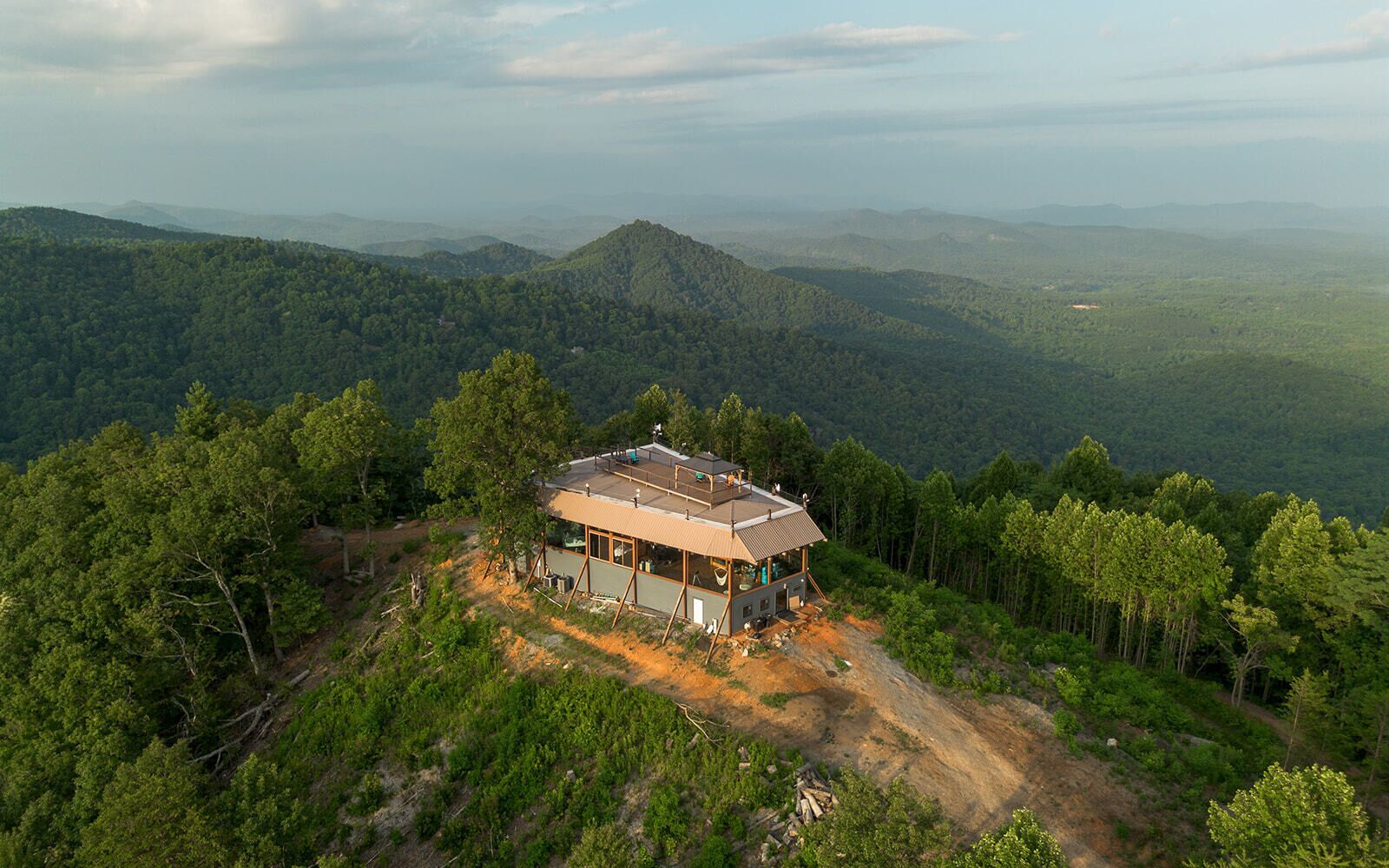 Uma cabana com um alpendre espaçoso, rodeada por uma floresta densa e montanhas.