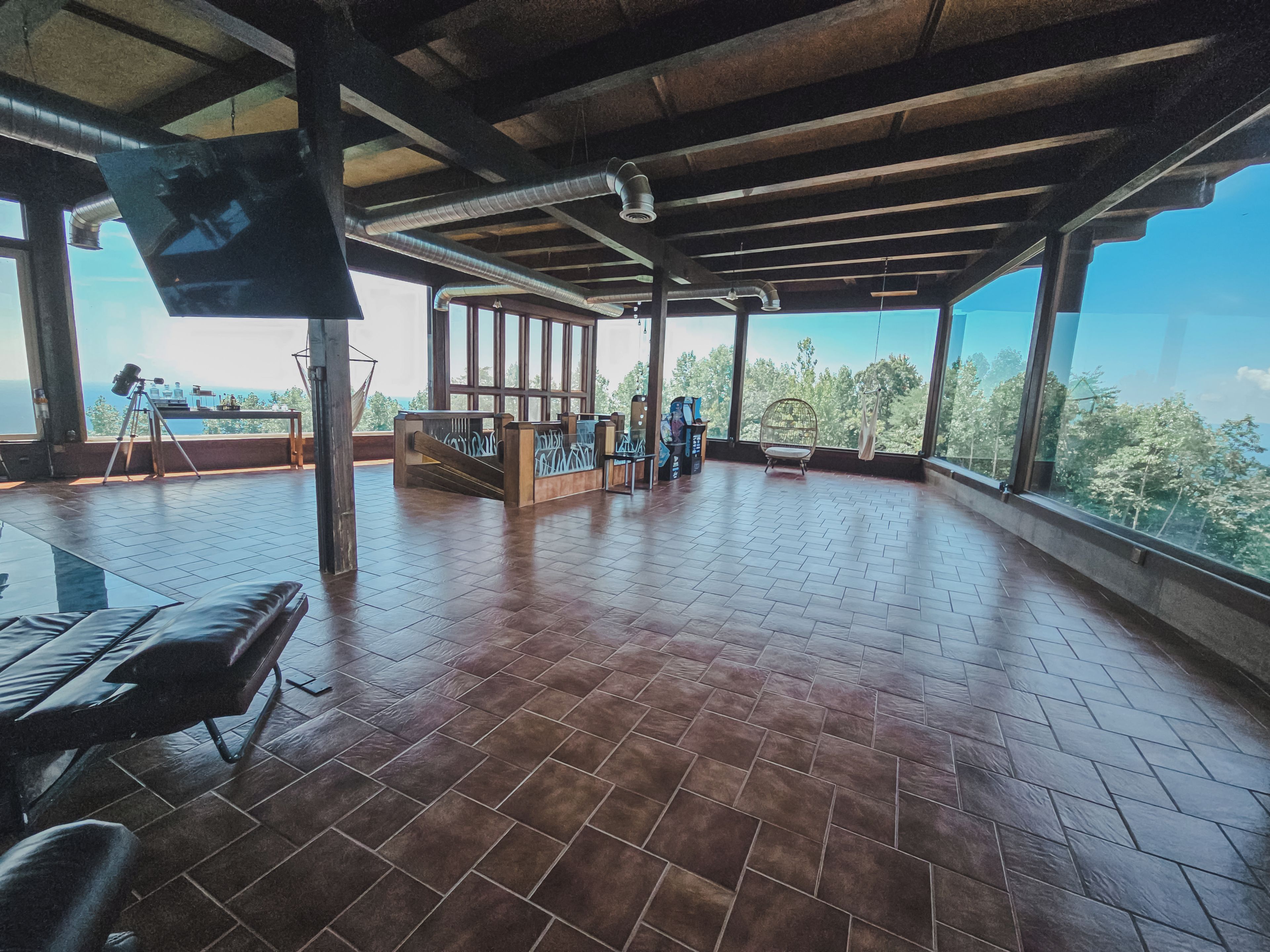 Quarto espaçoso com piso de azulejos, teto de madeira e janelas amplas com vista para o exterior.