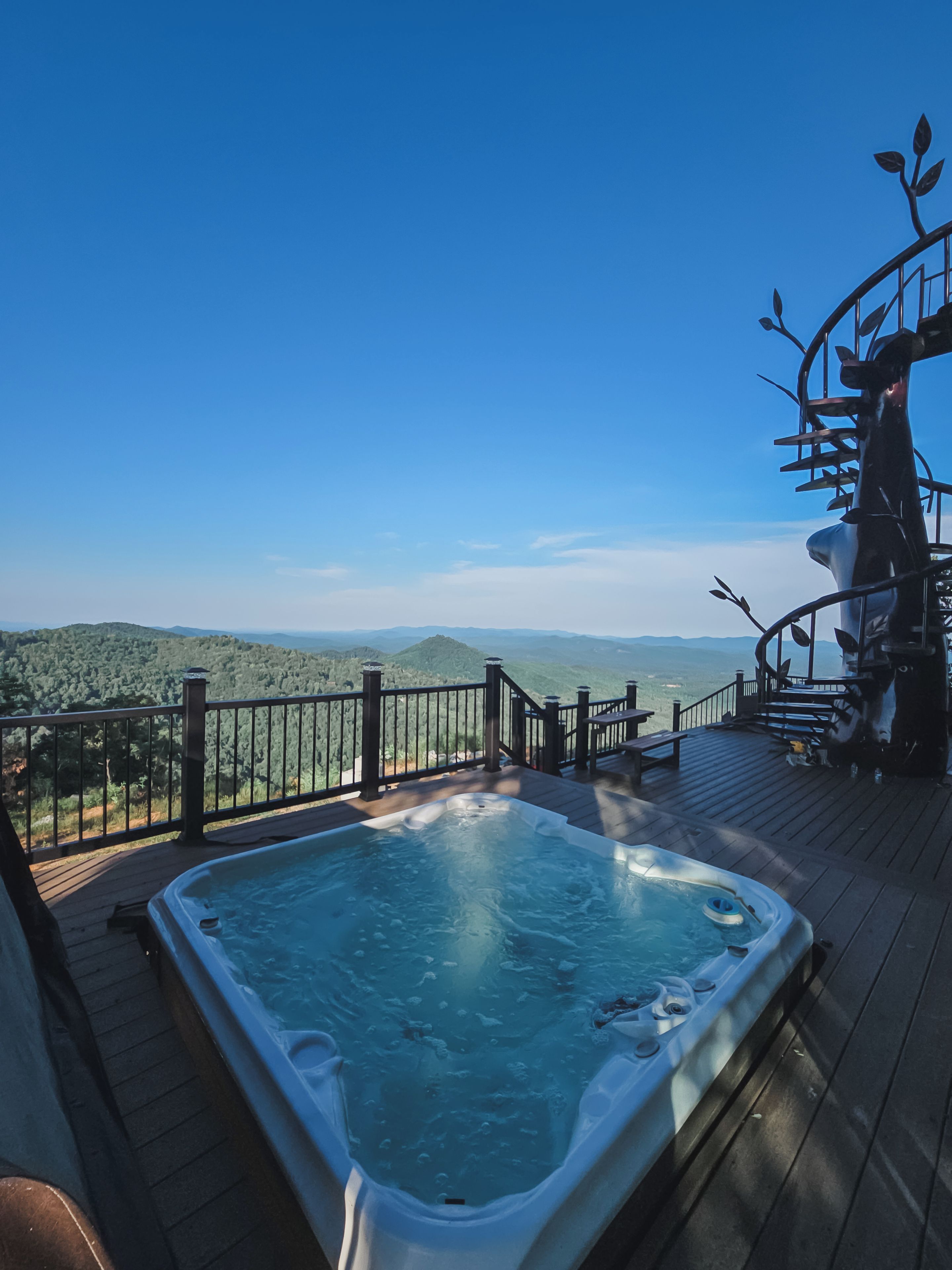 A hot tub on a wooden deck with a view of a forested mountain range.