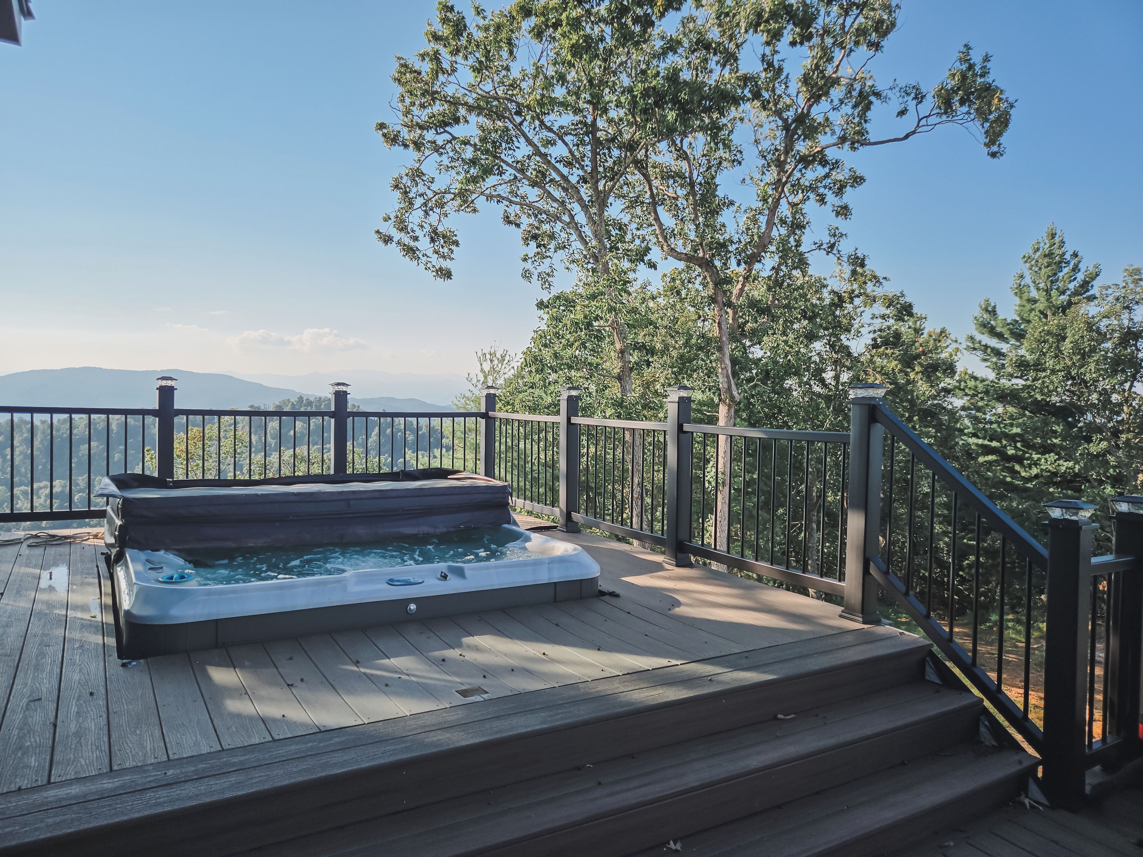Un jacuzzi en una terraza de madera con baranda metálica, con vistas a un paisaje montañoso.