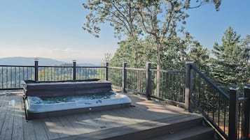 Un jacuzzi en una terraza de madera con baranda metálica, con vistas a un paisaje montañoso.