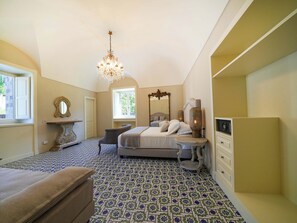 Un dormitorio con cama, una silla, tocador con espejo y candelabro.