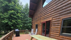 A wooden deck with picnic tables and a grill, surrounded by trees. - Serene 4-bedroom house in the beautiful White Mountains. (Haverhill)