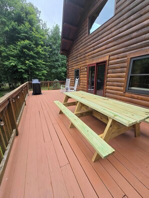 A wooden deck with picnic tables and a grill, surrounded by trees. - Serene 4-bedroom house in the beautiful White Mountains. (Haverhill)