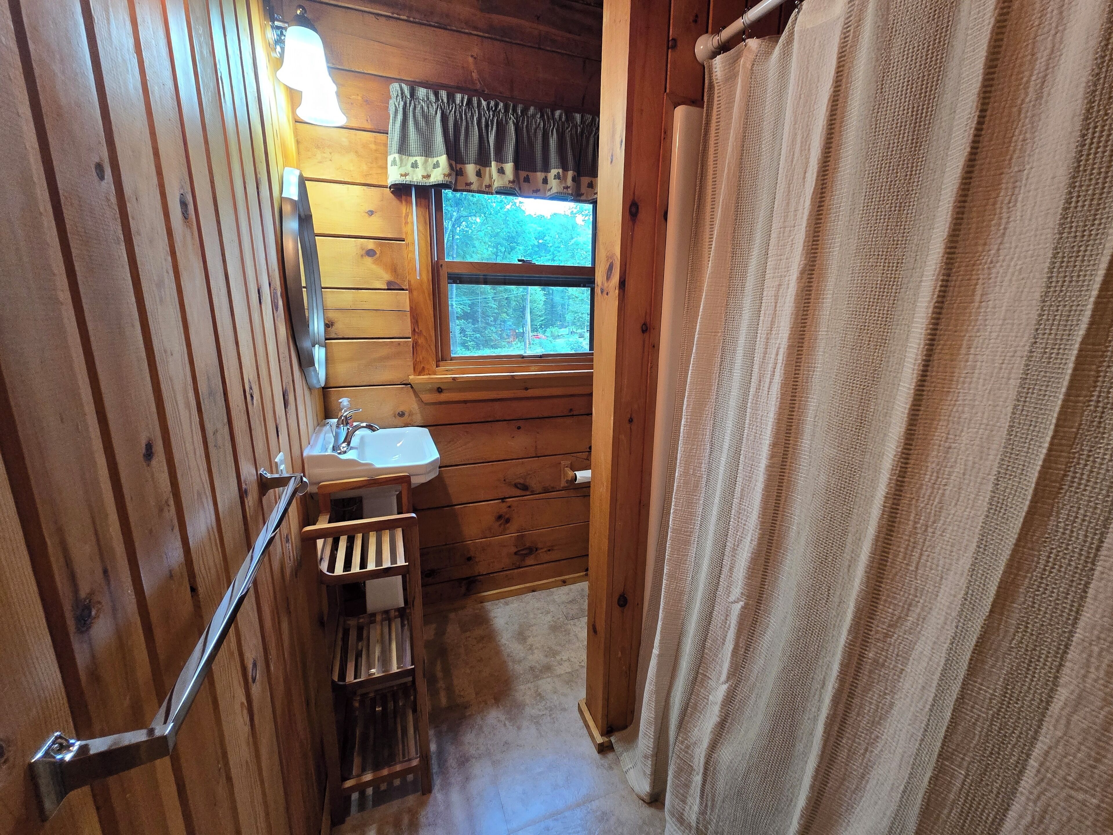 Ein Badezimmer einer Holzjagdhütte mit Fenster, Waschbecken und Handtuchhalter.