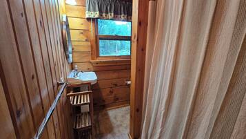 Ein Badezimmer einer Holzjagdhütte mit Fenster, Waschbecken und Handtuchhalter.