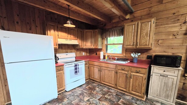 A wooden cabin kitchen with a white refrigerator, stove, and microwave. - Serene 4-bedroom house in the beautiful White Mountains. (Haverhill)