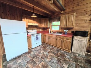Eine Holzhütte mit einer Küche, ausgestattet mit einem weißen Kühlschrank, Herd und einer Mikrowelle.