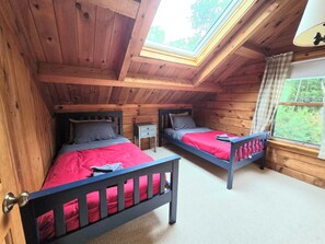 A bedroom with two beds, a skylight, and a window with a view of greenery. - Serene 4-bedroom house in the beautiful White Mountains. (Haverhill)